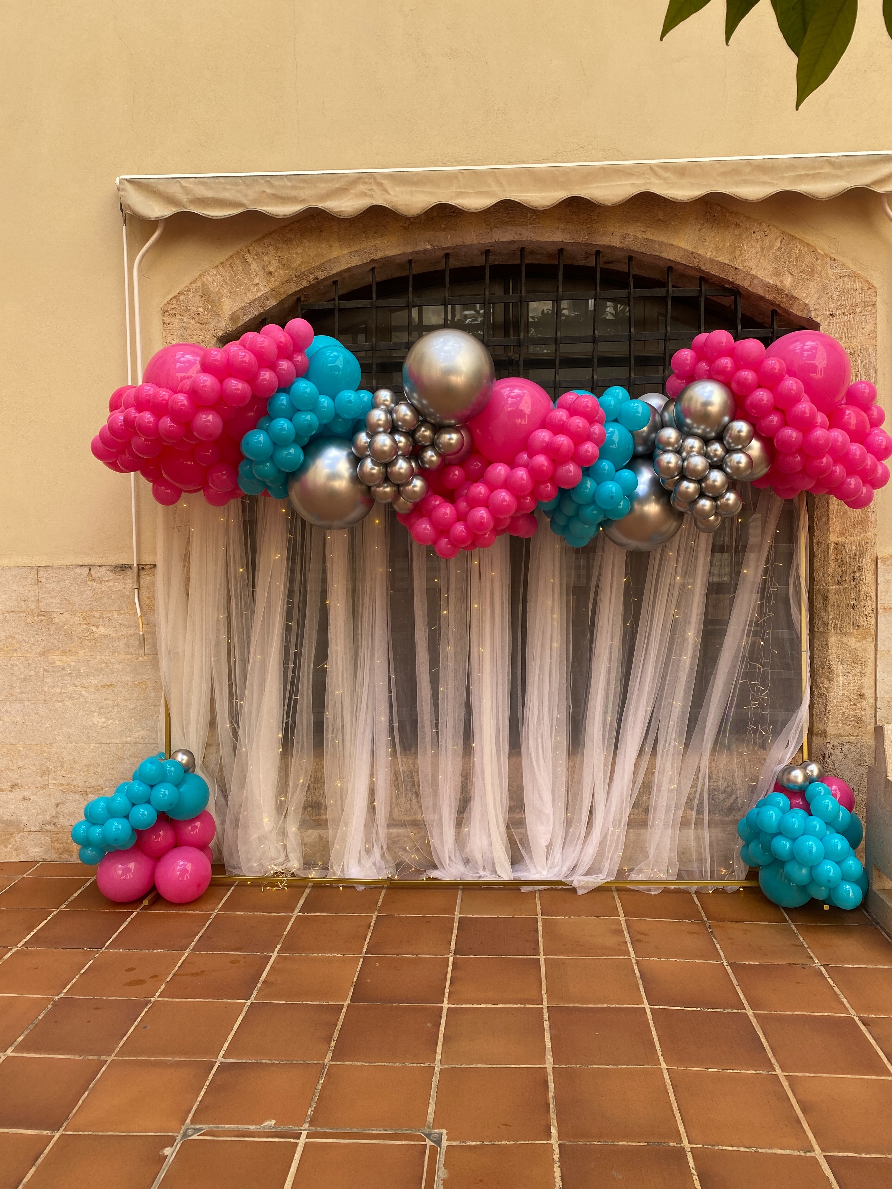 Rincón de graduación con cortinas y globos en tonos fucsia, azul y plata