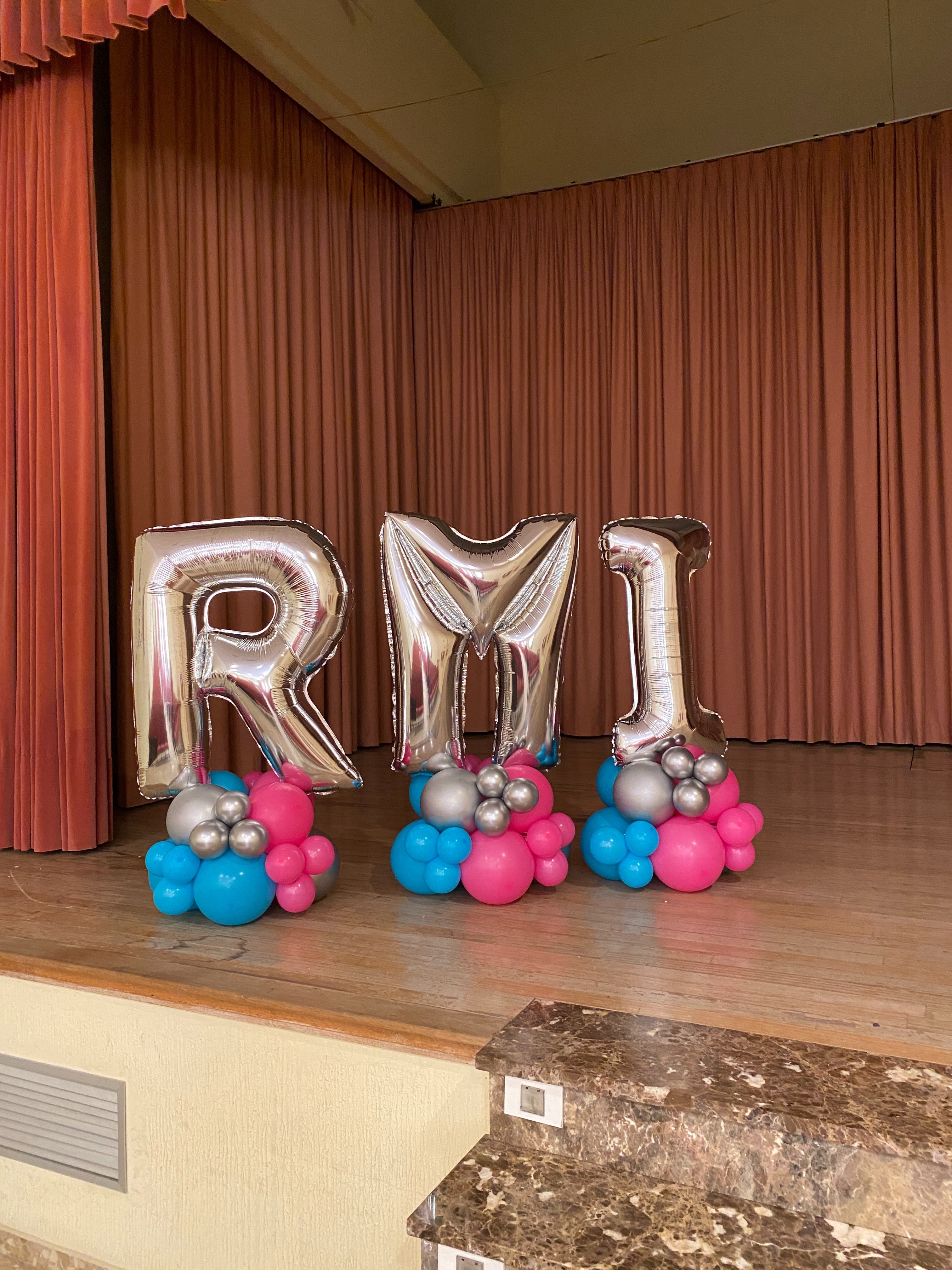 Escenario de graduación con letras grandes y globos azules y fucsias