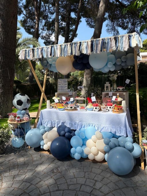 Mesa dulce exterior de comunión con globos azules, blancos y crema y detalles de fútbol