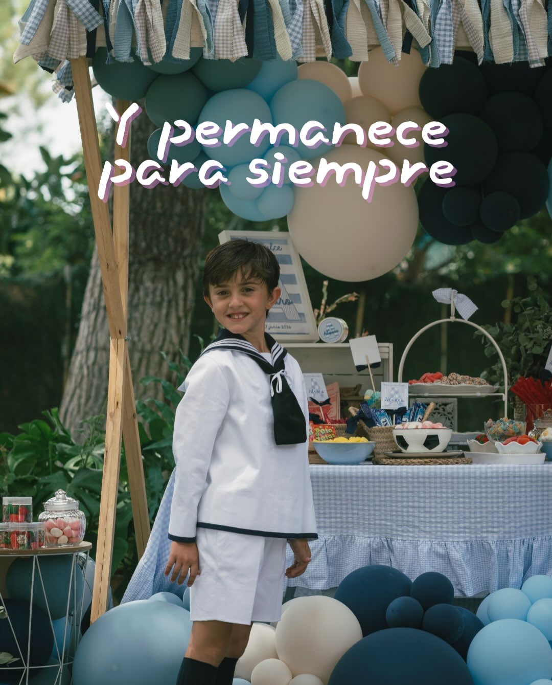 Álvaro delante de la mesa dulce de comunión con globos azules, blancos y crema