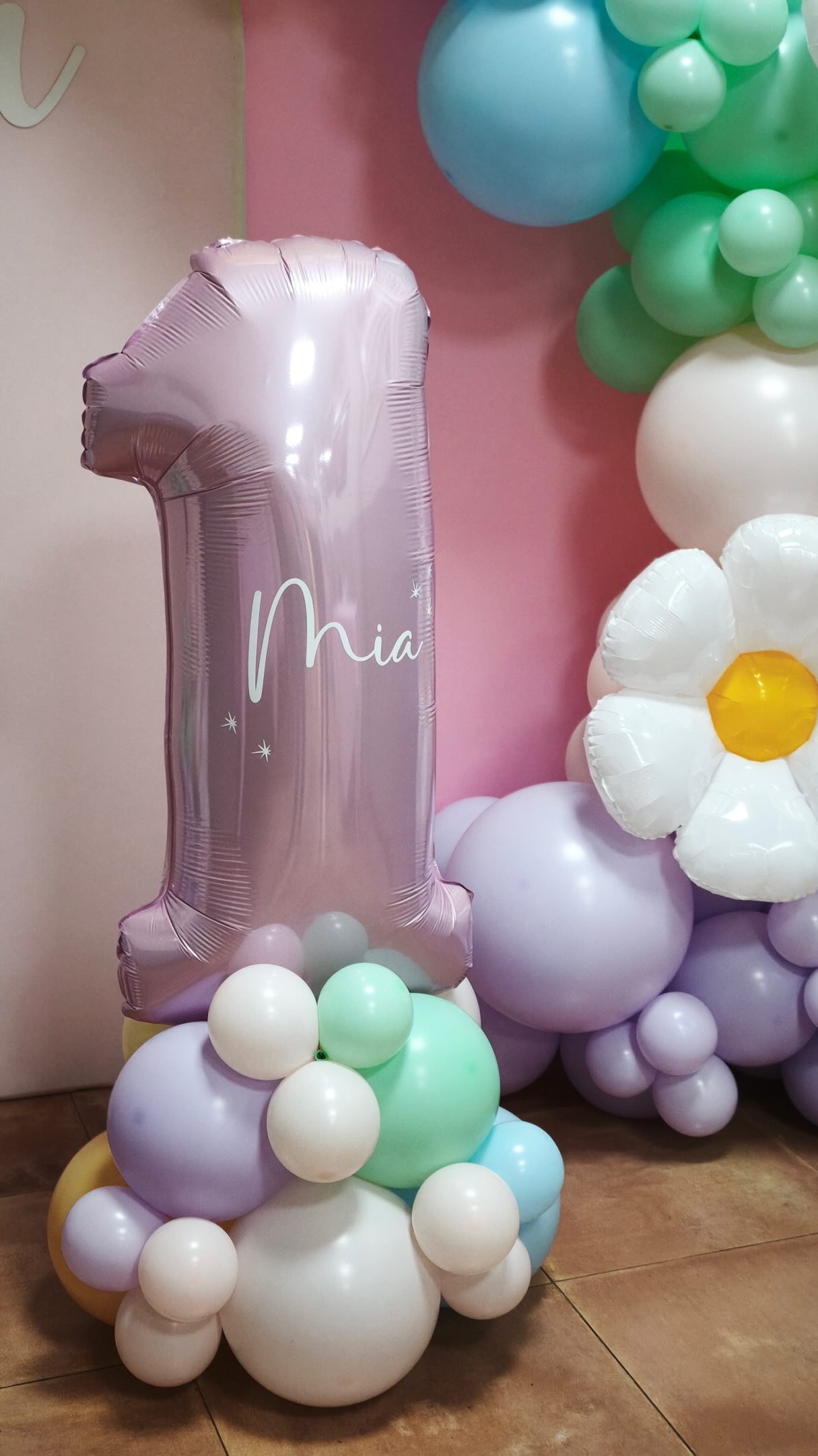 Photocall de primer cumpleaños con número 1 rosa y globos pastel en lila, verde, azul y blanco