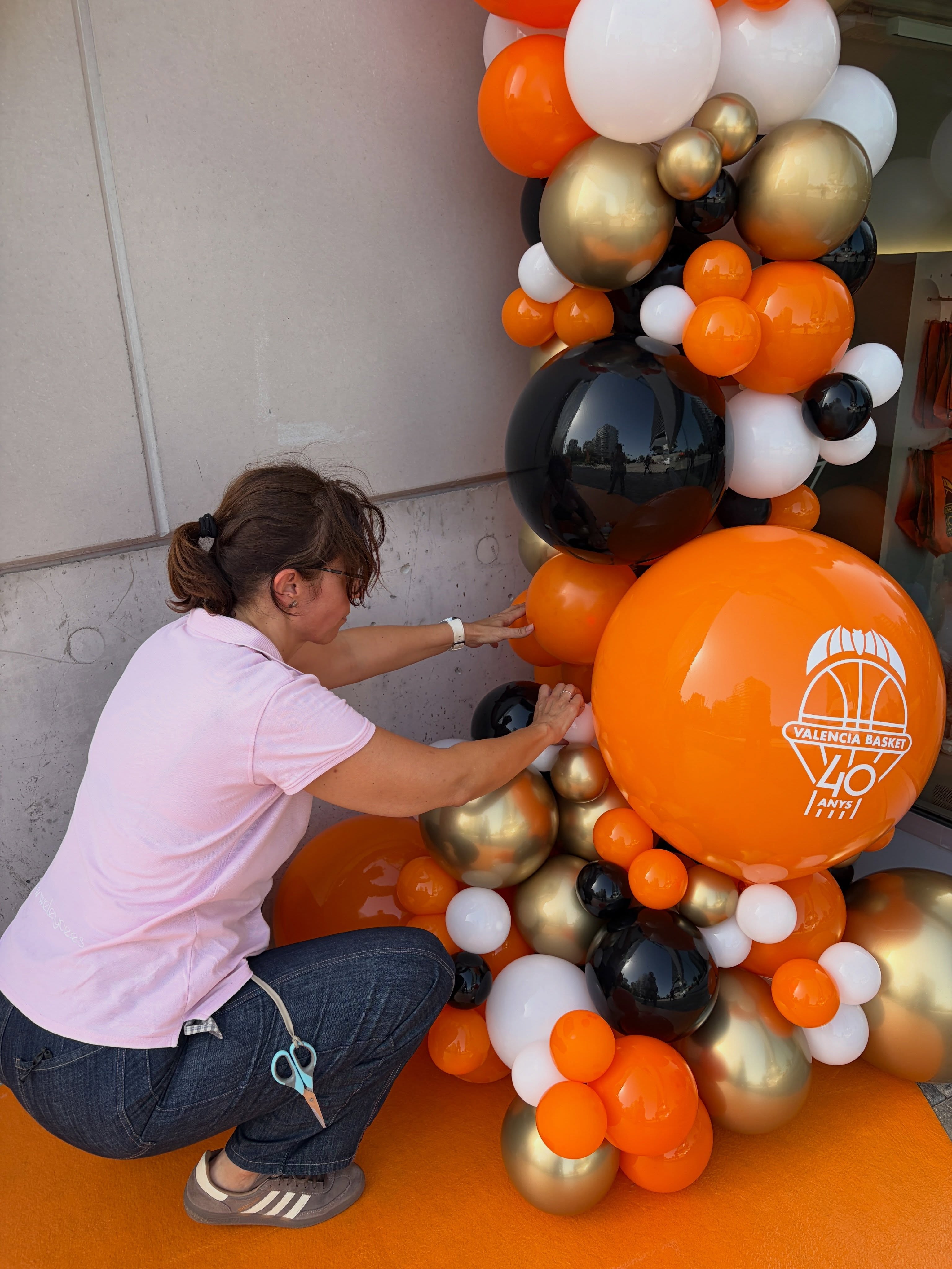 Integrante del equipo ajustando globos naranjas, negros, blancos y dorados del photocall