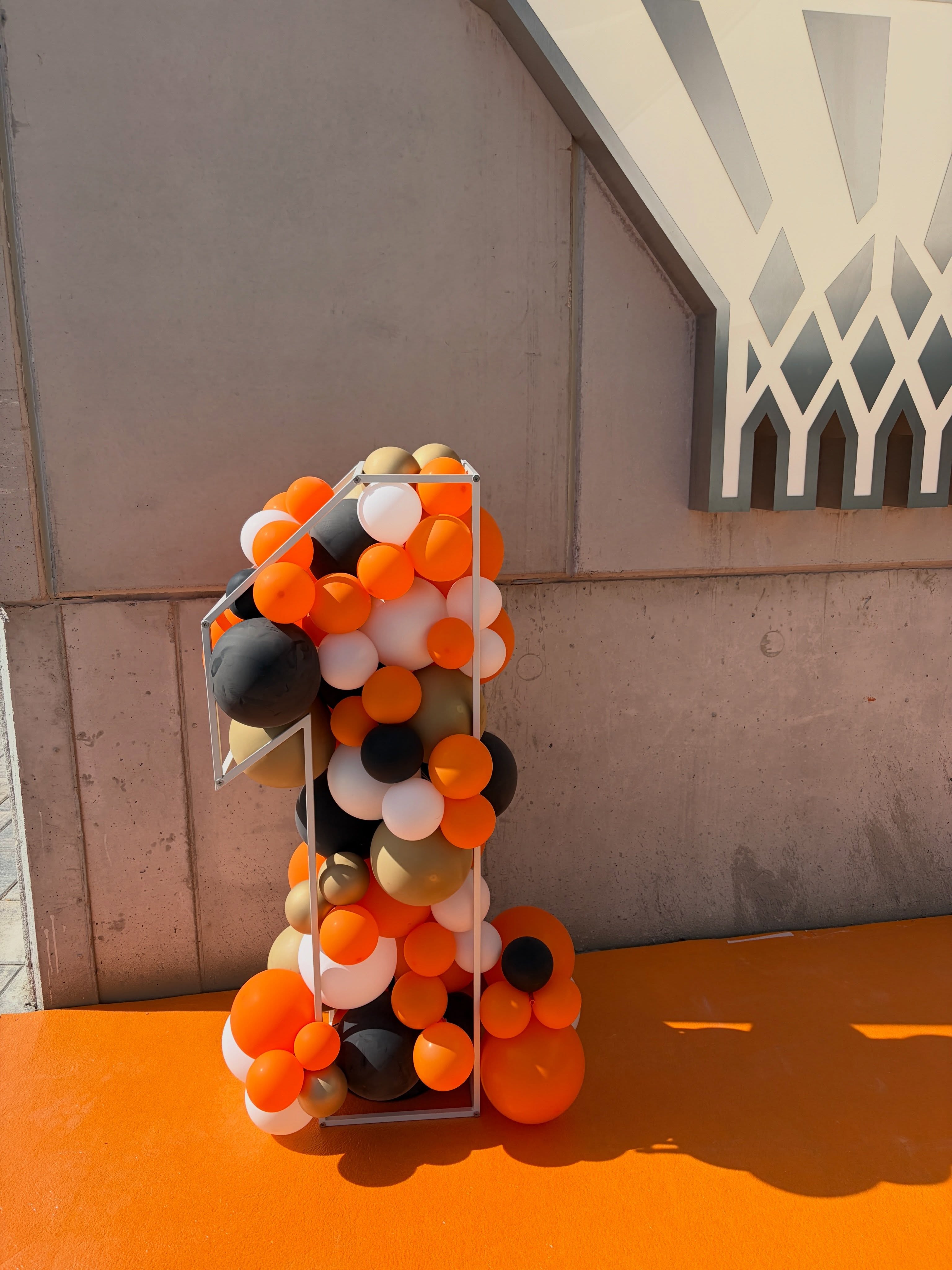 Estructura con forma de número 1 rellena de globos naranjas, negros, blancos y dorados