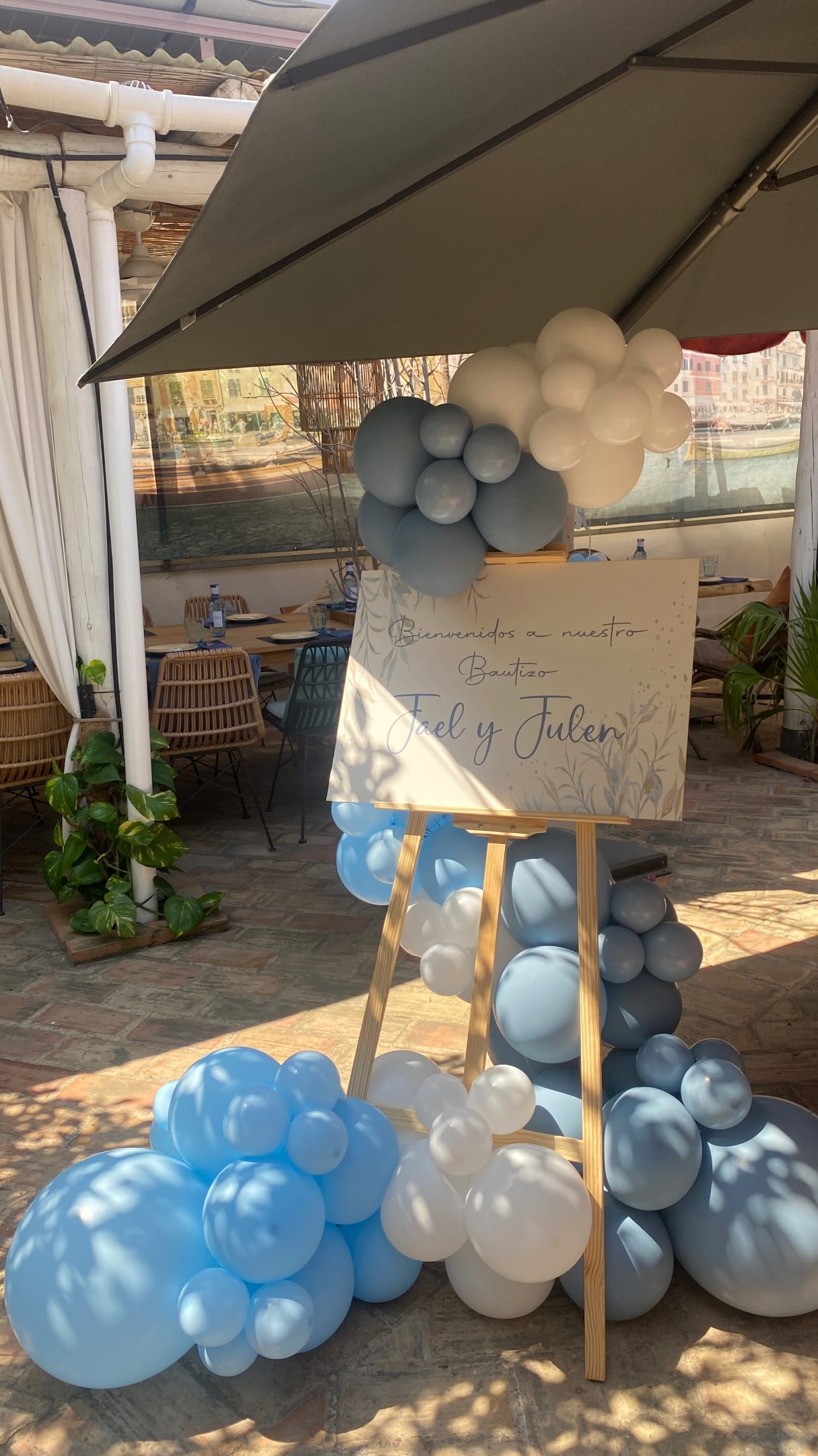 Cartel de bienvenida para un bautizo en Cocoa Patacona con globos azules, grises y blancos