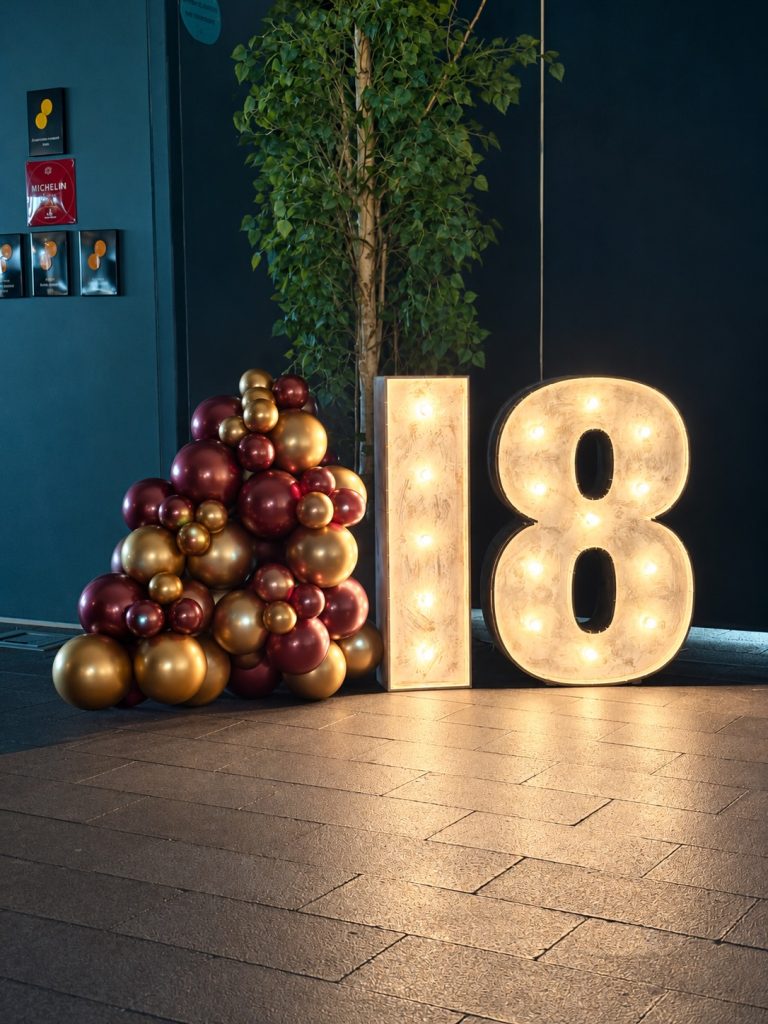 Número 18 luminoso junto a globos chocolate, burdeos y dorados en Veles e Vents