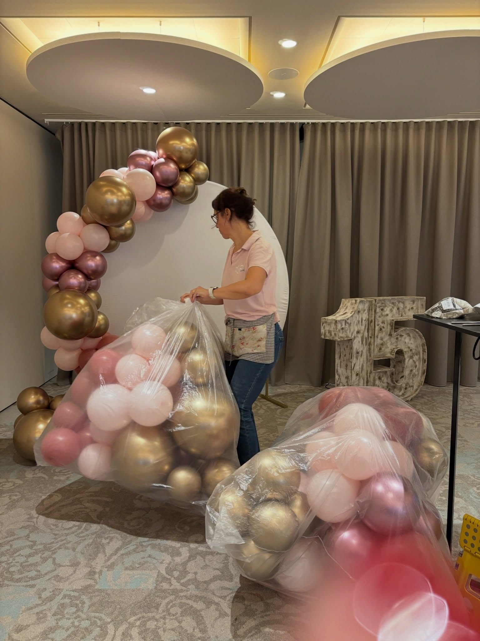Equipo de montaje preparando un arco de globos rosas y dorados para un 15 cumpleaños