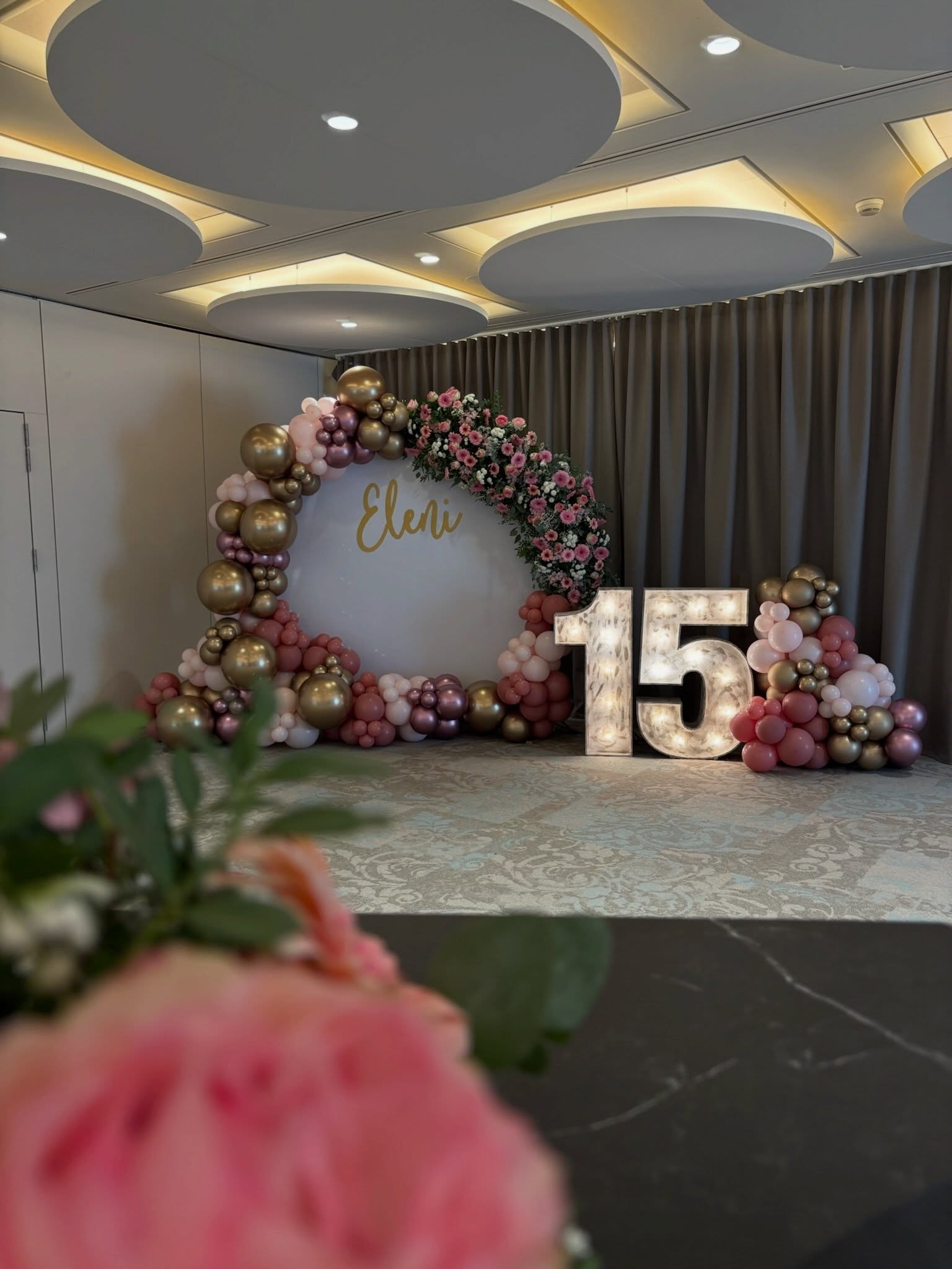 Decoración de 15 cumpleaños con globos rosas y dorados, flores y número luminoso